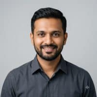 Professional headshot of an Indian architect in his late thirties wearing a dark shirt, photographed against a neutral light grey background.