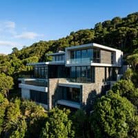 A small project thumbnail of a modern hillside villa with a flat roof, glass walls and stone cladding, surrounded by dense greenery.