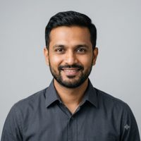 Professional headshot of an Indian architect in his late thirties wearing a dark shirt, photographed against a neutral light grey background.